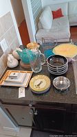 Overview of assorted kitchenware on counter including bowls, plates, pitcher, banana stand, ceramic swan containers