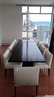 Overview of rectangular walnut finish table top with ten white leather chairs around it
