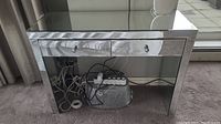 Photo shows mirrored hall table front view with two drawers, cables and power strip underneath.