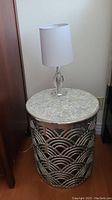 Side table with mother of pearl top and metal base displayed with glass table lamp on top, showing overall look of the lot.