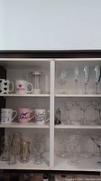 Wide shot of cabinet showing various mugs, a French press, and glassware shelves with stemmed glasses.
