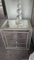 Front view of one mirrored side table showing three drawers, crystal-studded silver trim, and lamp base