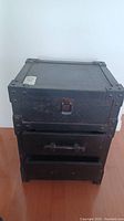 Front view of the black storage box showing the hinged lid with metal latch and two drawers below.