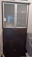 Front view of the storage cabinet showing frosted glass top doors, file drawer, and bottom cabinet doors closed.