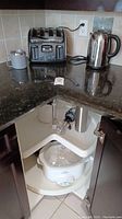 View of corner kitchen counter featuring Avante Deluxe 4-slice toaster, stainless steel electric kettle, small popcorn popper, and white Crock-Pot slow cooker in cabinet below.
