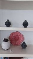Four pottery vases displayed on shelves and pink flower-shaped decorative plate.