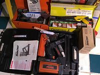 Ramset TF1100 power actuated fastening tool in black carrying case with charger, powder charges, manual, and orange charger box with powder cartridges visible.