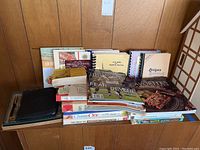 Multiple cookbooks and magazines stacked on a table including Sports Illustrated, vintage Baltimore Clippers programs, and a black CD case organizer.