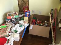 Overall view of Christmas decorations including ornaments, figurines, tree skirt, and string lights packed in boxes and on a table.