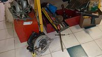 Wide view of the lot showing two circular saws, a four foot level, various tools in boxes, paint brushes and roller pads.