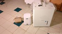 Wide shot of SoClean CPAP sanitizer next to Amazon Basics dehumidifier on tiled floor with small box and manual present.