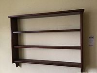 First wooden wall curio shelf with three levels, brown polished wood, mounted on wall.