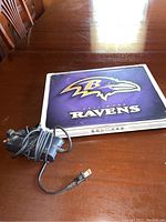 Closed Dell laptop with Baltimore Ravens cover and power adapter placed beside it on a wooden table.