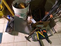 Overview of drywall mud tray, mud hawk, sponge hawk, mixing paddle, hammer, manual drill, handsaw, and pipe clamps in box and leaning.