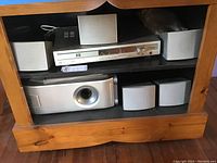 Front view showing Fisher DVD player receiver JCX-TS750A on upper shelf and five satellite speakers plus subwoofer below in wooden shelf.