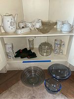 Various vintage dishes including clear glass pumpkin candy dish, bowls with blue rims, green glass Christmas tree candy dish, and ceramic coffee mugs.