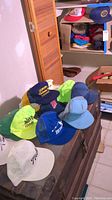 Multiple vintage hats displayed on a brown surface and shelving including neon green, blue, navy and white caps with embroidered logos.