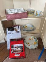 Various plates, bowls, packaged table protector, and folded tablecloth on white shelves