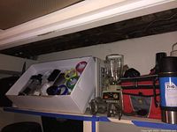 Magic Bullet blender with multiple colored cups inside a white box, vintage Osterizer blender base and glass pitcher, antique meat grinder, red and black soft sided lunch cooler bag, five thermoses