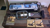 National Geographic Pro Series metal detector in original packaging, metal detector and two guide booklets visible on wooden surface.