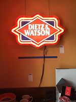Photo showing the Dietz & Watson neon sign lit up on a wall with visible power cord and hanging wires.