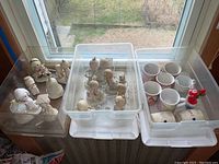 Photo of multiple Precious Moments porcelain figurines in plastic bin, placed on window ledge.