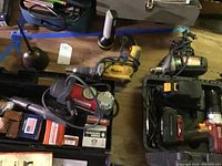 Photo showing Ramset stud driver, Milwaukee reciprocating saw, Chicago Electric drill in hard case with charger, oil can, flashlight, and Husky inflator on table.