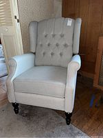 Front view of the light gray recliner armchair showing button tufted backrest and dark wooden legs.