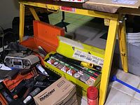 Photo showing sawhorse beneath a table cluttered with tools and a red toolbox, illustrating the working environment and scale of the sawhorses.