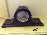 Front view of Seth Thomas mantel clock on yellow surface with winding key beside it.