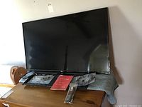 Full view of TCL 42-inch TV, visible screen, remote, power cord and wall mount parts on wooden table with protective cloth beneath.