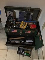 Photo of open metal green toolbox with tools packed inside, showing hammers in drawer and assorted tools in main compartment