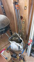Photo showing large bar clamps, 4 and 6 foot spirit levels, white cloth bag of small tools, and part of charcoal grill.