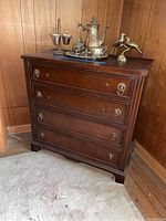 Full front view of the wooden dresser with four drawers, brass handles, and decorative molding under good lighting.