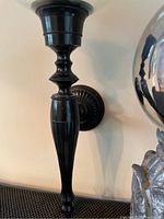 Close-up of the black metal wall-mounted candle lamp with decorative curvatures and round back plate