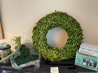 Photo showing green leafy wreath with metal hook, artificial moss in plastic, and some flower wire on table.
