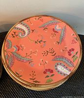 Top view of one coral colored plate with paisley and floral patterns, bamboo-style rim visible.