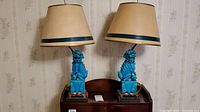 Pair of turquoise ceramic foo dog lamps with beige shades on wooden carved stands