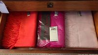 Three folded scarves—coral (left), fuchsia (center), light pink (right)—in a drawer.