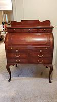 Front view of closed roll-top desk showing decorative inlay and brass hardware