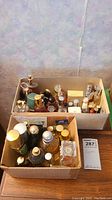 Two cardboard boxes filled with assorted perfume bottles on wooden table