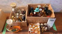 Overall view of two cardboard boxes containing assorted fragrance bottles and vials, plus two large decorative bottles at front
