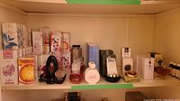 Shelf showing six sealed Aqua Allegoria boxes, red faceted bottle, white rounded bottle, tall blue box, green box, black container and green cloth