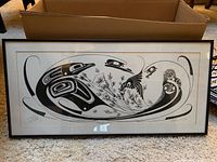 Framed indigenous black and white art print with abstract animal and human shapes, laid on carpet in front of cardboard box.