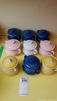 Wide shot of nine Le Creuset stoneware mini cocottes with lids in various colors arranged in three rows.