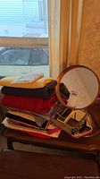 Mirror and stack of folded fabrics on wooden table by window
