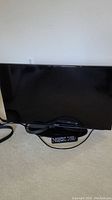 Black 40-inch Samsung flat screen TV sitting on carpeted floor with cables and remote underneath.