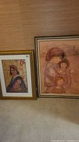 Full view of both framed artworks leaning against wall on carpeted floor.