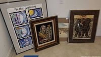 Four framed art pieces leaning against wall on carpeted floor