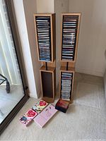 Full view of two wooden CD storage towers with multiple CDs vertically stored inside. Four boxed items placed on floor in front, one being I Love Lucy DVD box set.